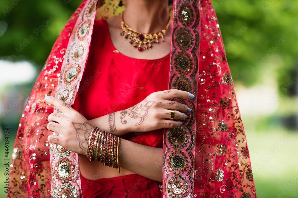 partial view of young indian bride in red sari adjusting headscarf with ornament