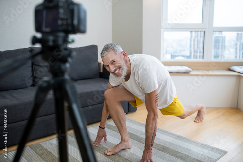 A mature man in white tshirt recording an online yoga tutorial