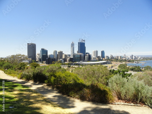 Skyline of a metropolitan area against a clear blue sky. Green vegetation and sinuous concrete sidewalk in the foreground. View of Perth and Swan River from  Kings Park, Western Australia.
