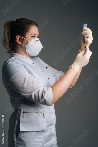 Veretical studio shot of nurse in white gloves and face mask holding and filling up vaccine to syringe on black isolated background. Doctor preparing to give injection of coronavirus vaccine. photo