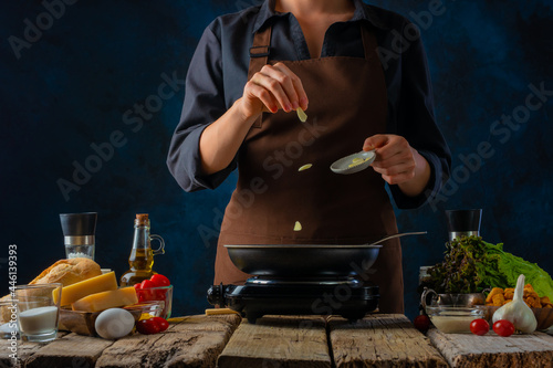 The chef prepares a classic Caesar salad. There is a frying pan on the table. The cook throws pieces of garlic at her. Levitation. Many ingredients for the salad are spread out on the table.