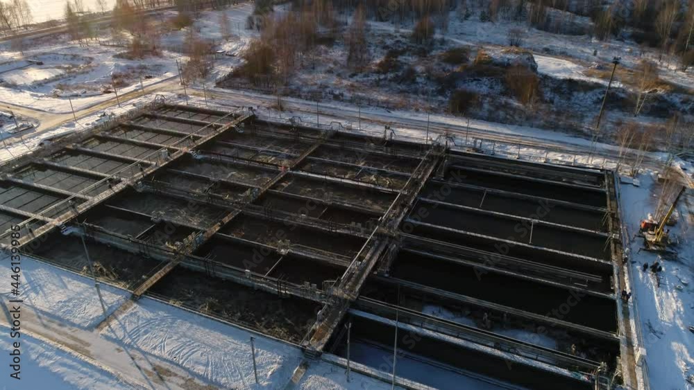 Group of pools with aerated water and bridges at treatment plant on snowy hill at sunset in winter bird eye view Group of pools with aerated water and bridges at treatment plant on snowy hill at sunset in winter bird eye view