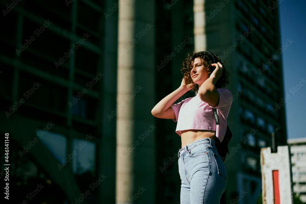 Portrait of a girl with curly hair dressed casually standing outdoors and looking away.