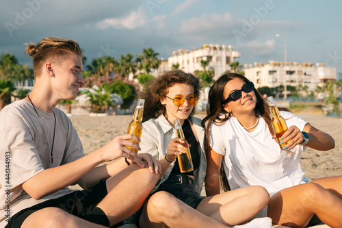 Young happy friends doing picnic seaside close-up portrait. Group of people sitting on the beach, eating pizza and drinking beer together. Summer spending time outdoor concept.