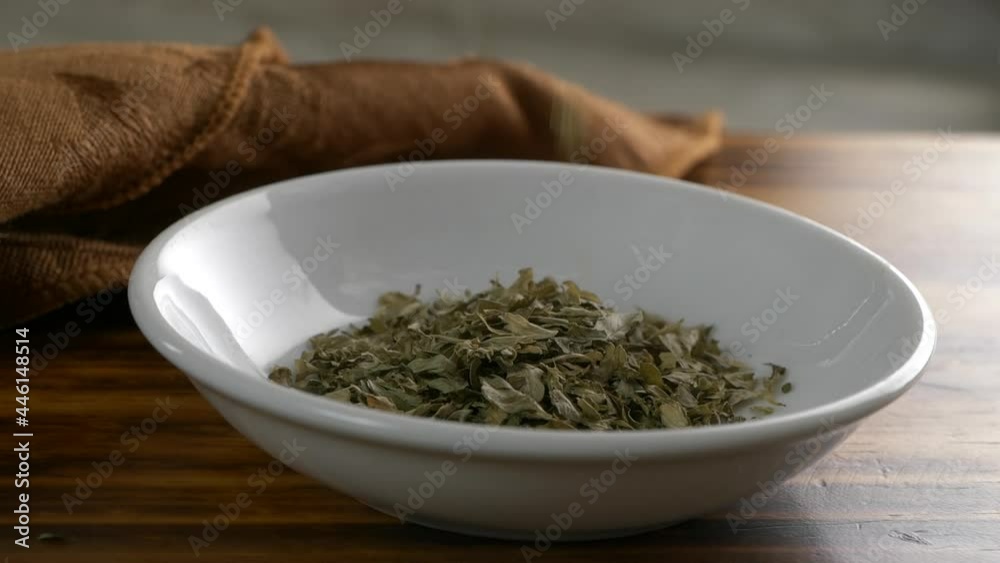 Dried parsley flakes falling into a small dish super slow motion Dried parsley flakes falling into a small dish super slow motion