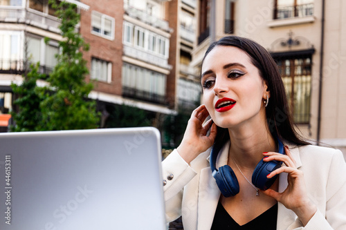 Young brunette caucasian woman working in laptop with bue headphone and tying his hair photo