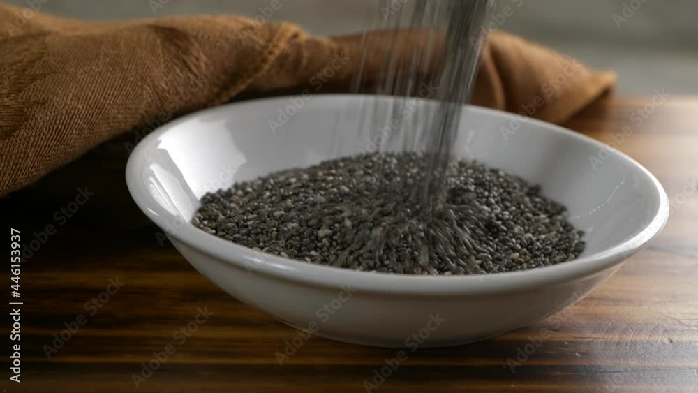 Pouring black chia seeds into a small bowl, backlit super slow motion 
