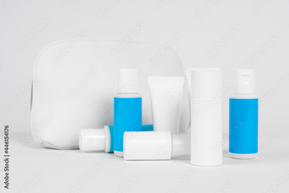 Small tubes and bottles made of recyclable plastic with products for skin care or cleansing, stand on white background with cosmetic bag for traveling, front view, copy space.