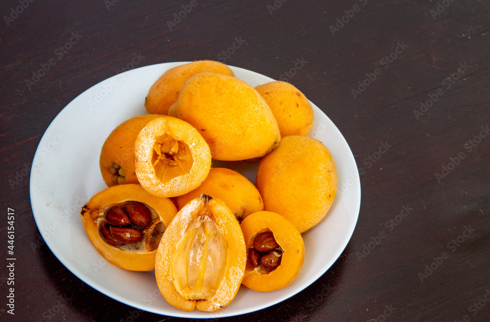 Ripe loquats in white dish on rustic wooden background with cut showing inside with seeds. (Eriobotrya japonica). loquat fruits Ripe loquats in white dish on rustic wooden background with cut showing inside with seeds. (Eriobotrya japonica). loquat fruits