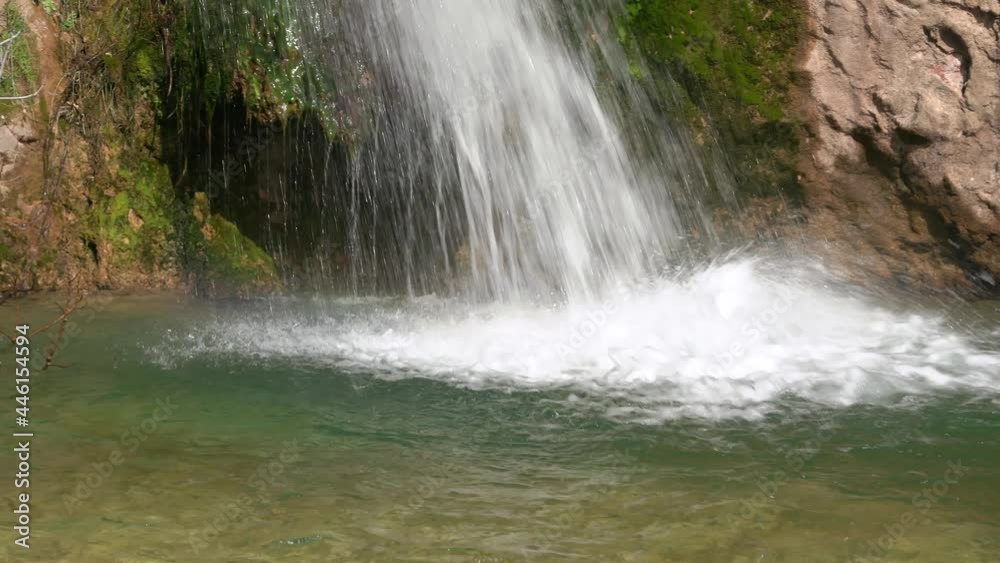 Wonderful jets of waterfall run down into small transparent lake near old stone cliff on sunny spring day close view zoom IN Wonderful jets of waterfall run down into small transparent lake near old stone cliff on sunny spring day close view zoom IN