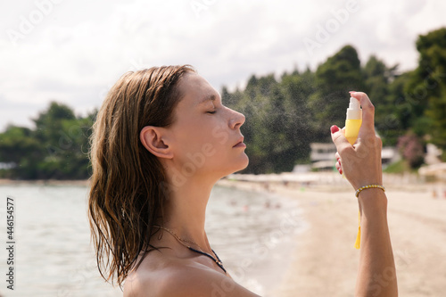 Woman spraying facial mist on her face, summertime skincare concept 