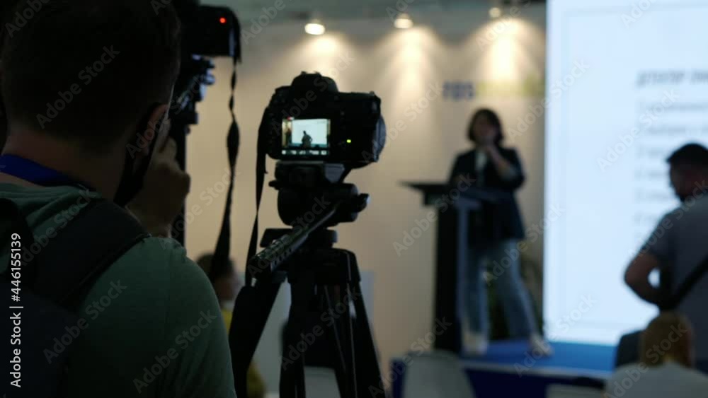 A videographer is filming the speakers in the conference room. A videographer is filming the speakers in the conference room.