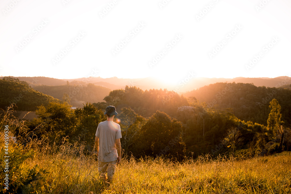 Young man walking through the grass with mountains and sunset in the background.