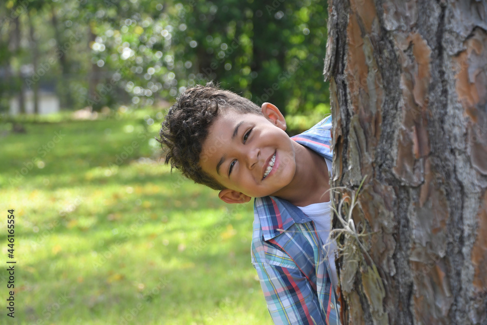 Smiling boy looking out from behind a tree.