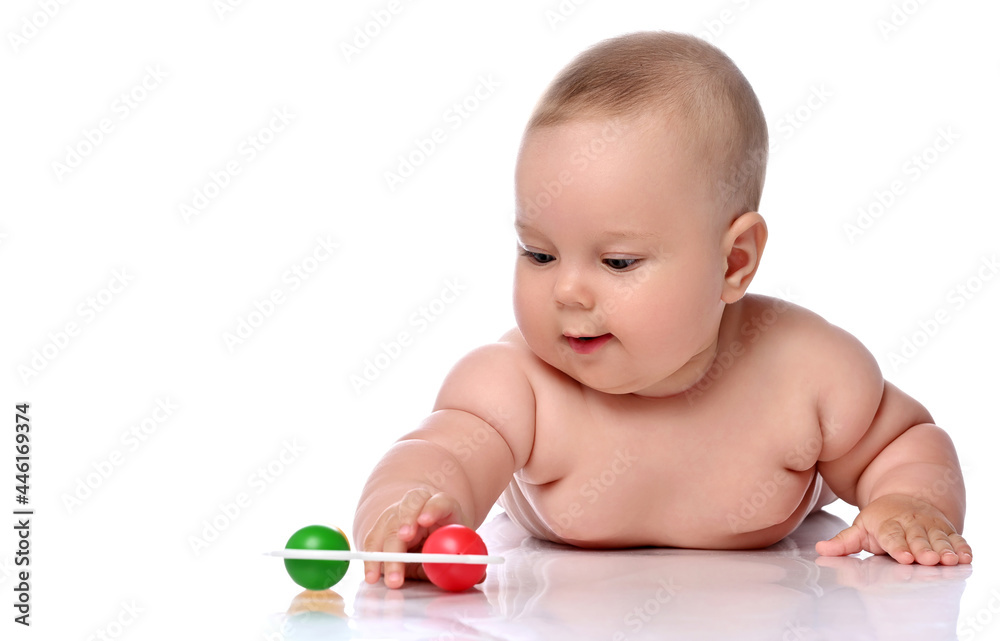 Smiling infant child baby girl kid in diaper is lying on her stomach playing with rattle, touching with hand isolated on a white background