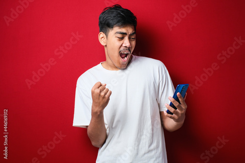 Young indian man using smartphone screaming proud and celebrating victory and success very excited, cheering emotion