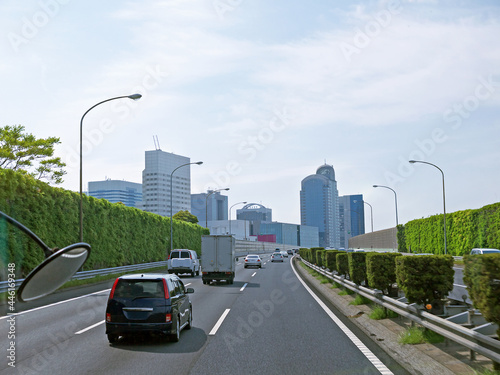 Entering Tokyo by highway with tall green Overgrown noise barriers with grass on roadsides  distant downtown Office buildings in background  Japan