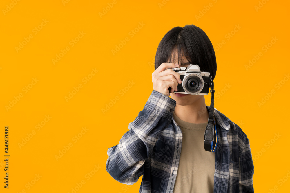 Asian teen girl photographer taking a picture and looking viewfinder on vintage photo camera, isolate on yellow background Asian teen girl photographer taking a picture and looking viewfinder on vintage photo camera, isolate on yellow background