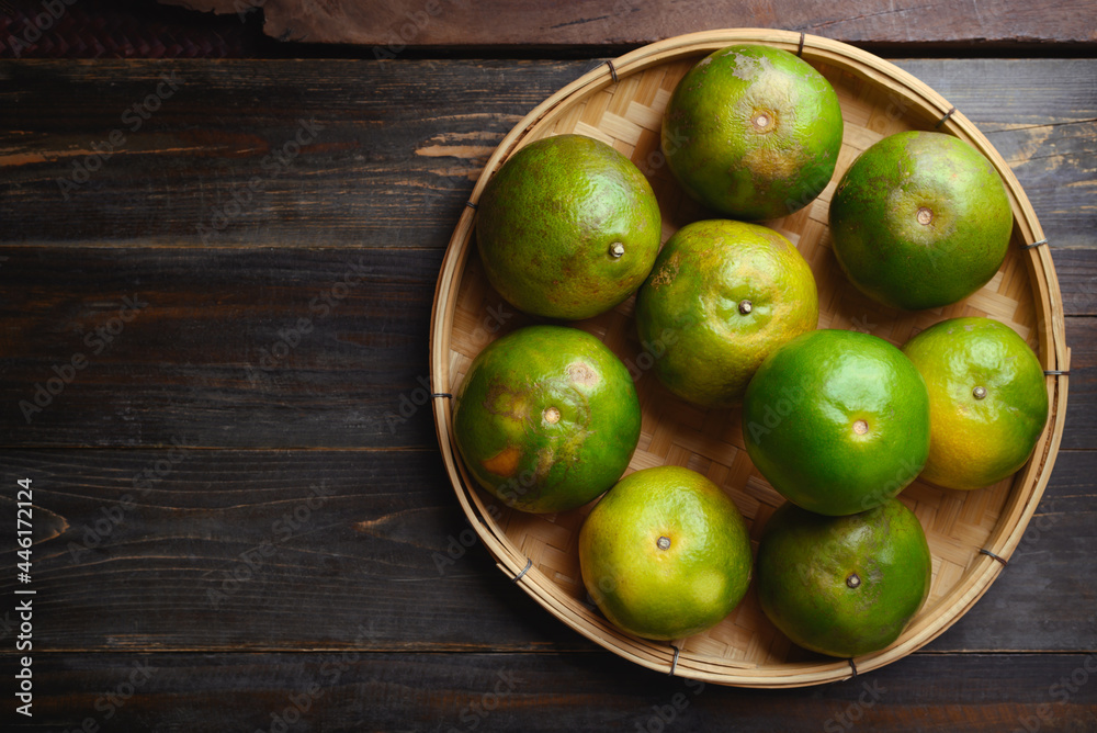 Green tangerine orange fruit in a bamboo basket on wooden background, Table top view Green tangerine orange fruit in a bamboo basket on wooden background, Table top view