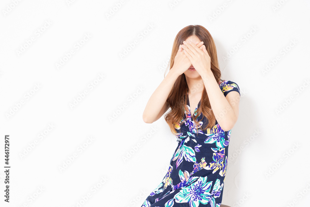 白い壁の前で、顔を隠す、青いワンピースを着た若い女性 白い壁の前で、顔を隠す、青いワンピースを着た若い女性