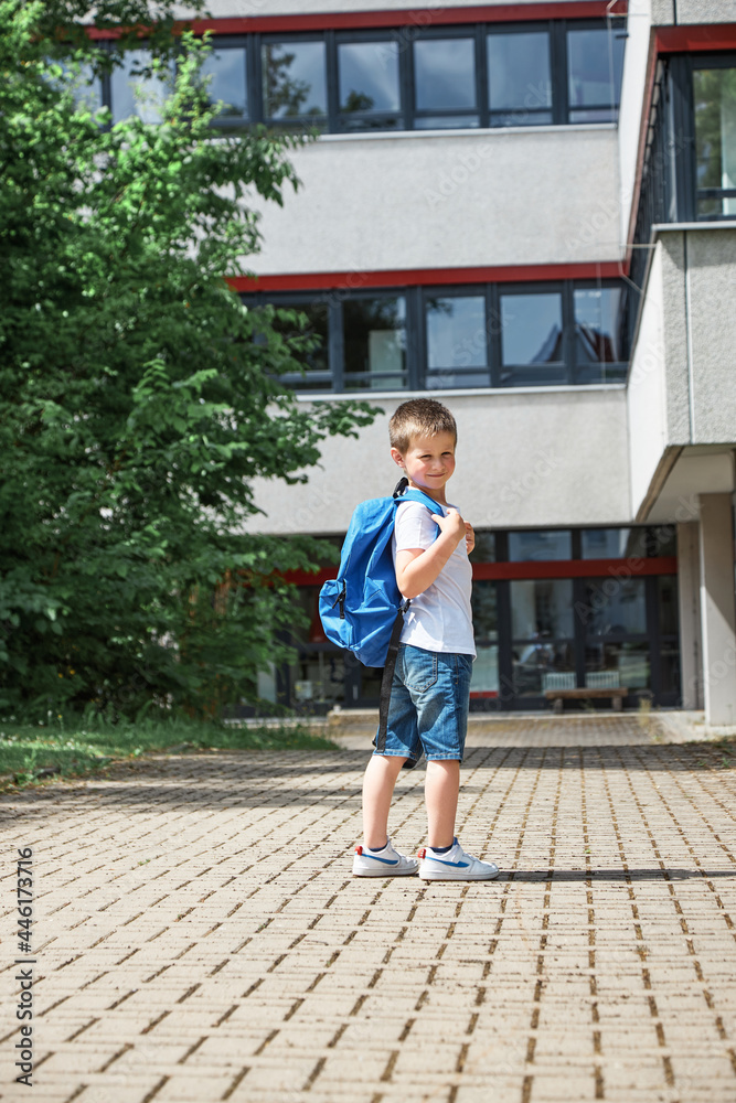 Adorable boy goes to school after vacation. A schoolboy with a backpack is standing and waving to his parents. Back to school, start of the school year