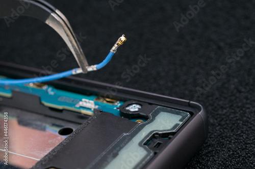 close-up of disconnecting the contact wire with tweezers, phone repair, antenna