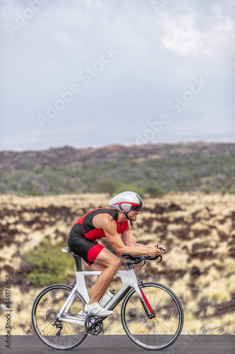 Triathlon time trial competition triathlete man cyclist riding road bike in Hawaii race cycling uphill in tough race in volcanic landscape. Fitness active lifestyle.