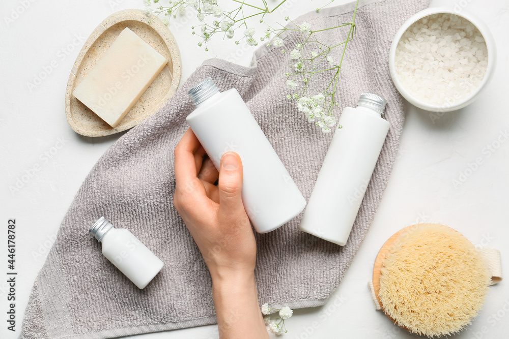 Female hand with bottle of cosmetic products and bath supplies on light background