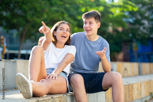 Young lady and young man are sitting on the step and pointing with fingers © JackF