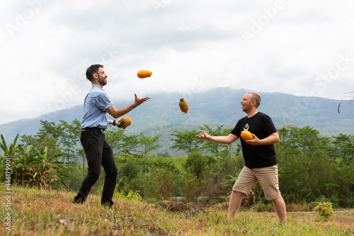 Two caucasian hipsters play with papaya and pineapple outdoors, friend, joke, vegetarian