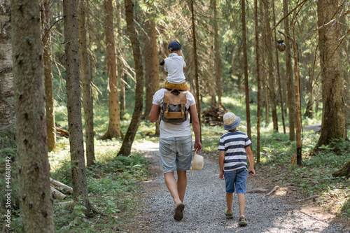 Fototapeta Naklejka Na Ścianę i Meble -  Backview of man walking alone the leane in forest with two sons. One boy is sitting on his shoulders