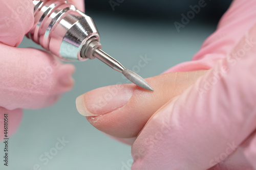 Removing the nail plate with a milling machine. Manicure process in beauty salon  cleaning of nails by a milling cutter. Manicurist filing client s nails at table  close up. Shallow depth of field