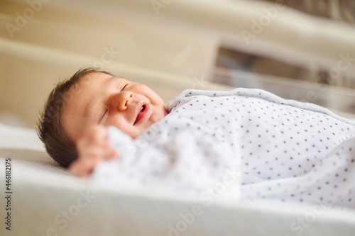 Close up portrait of newborn smiling baby girl. Infant lying in crib in hospital. New born baby second days of life in hospital. Healthcare newborn prenatal concept.