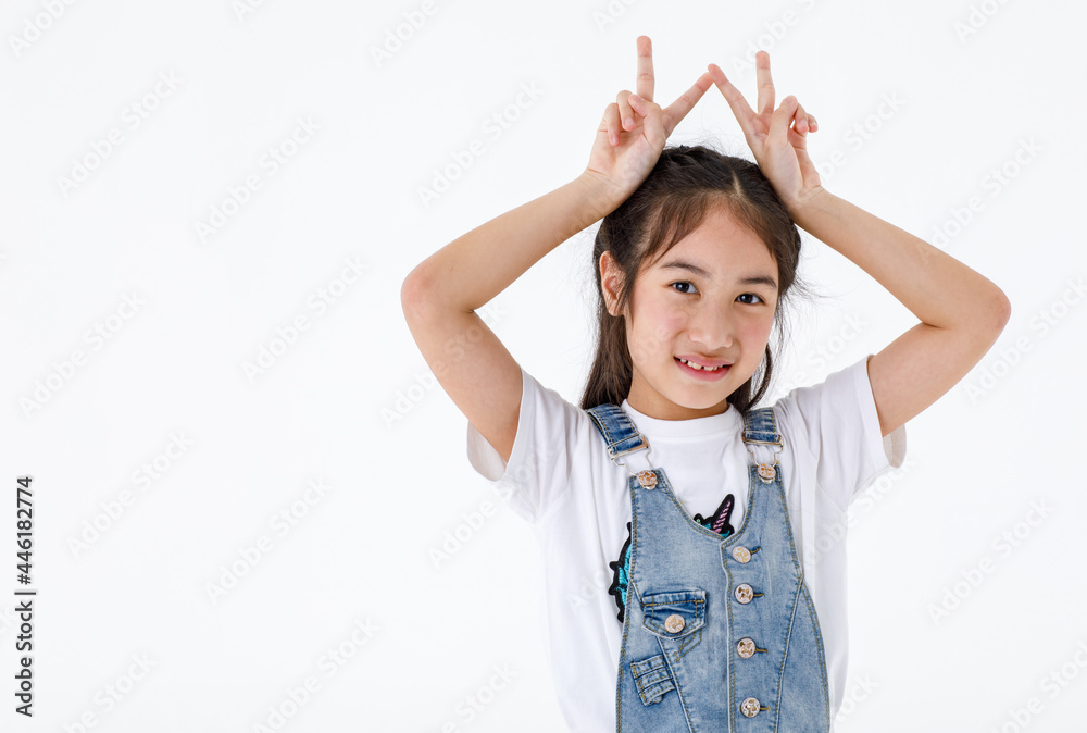 Portrait close up isolated studio shot of young pretty cute girl in jeans denim skirt overalls standing look at camera hold hands up overhead show two fingers peace sign in front of white background Portrait close up isolated studio shot of young pretty cute girl in jeans denim skirt overalls standing look at camera hold hands up overhead show two fingers peace sign in front of white background