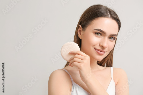 Beautiful young woman with makeup sponge on grey background