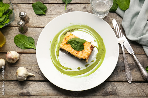 Plate with tasty green lasagna on wooden background