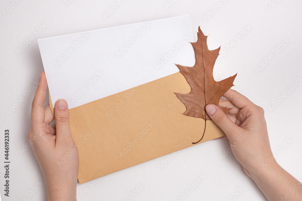 female hands holding an envelope with a blank letterhead about autumn leaf, get sad news, message, autumn discounts and sales, invite for shopping, copy space, mock up for design