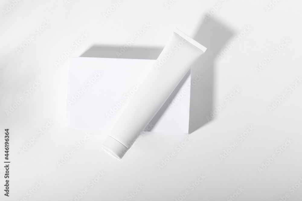 White cosmetic tube on a stand with leaves and shadows. Toothpaste, face and body cream. Female cosmetic tube with skin care product. Organic cosmetics. Copy space. White cosmetic tube on a stand with leaves and shadows. Toothpaste, face and body cream. Female cosmetic tube with skin care product. Organic cosmetics. Copy space.