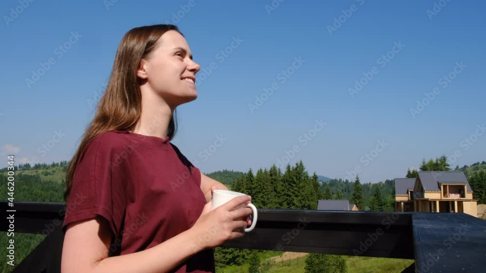 Travelling beautiful smiling young caucasian woman 20s drink hot coffee or tea stand in sunshine at summer morning day, enjoy warmth of sun on her skin. Concept travel wanderlust and adventure mood