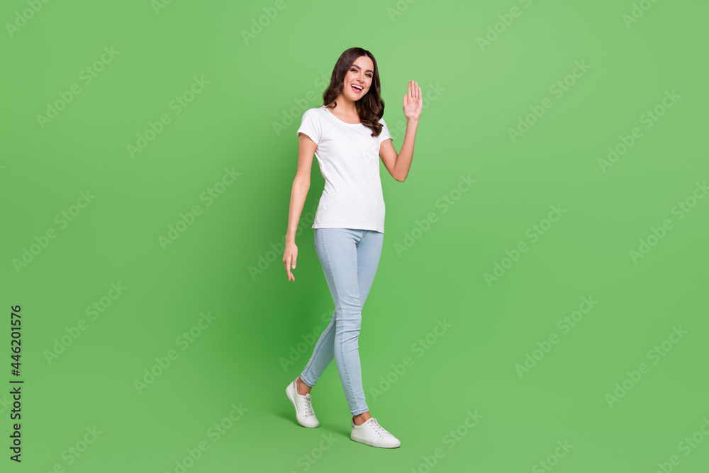 Full length photo of cool brunette millennial lady go wave wear t-shirt jeans isolated on green color background Full length photo of cool brunette millennial lady go wave wear t-shirt jeans isolated on green color background