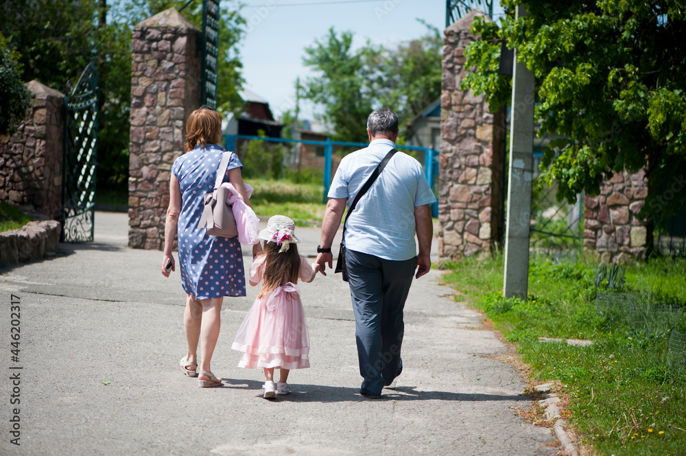 family walking in the park. mom dad and little girl walking holding hands. back view. daughter in a pink dress. friendly loving family concept, love. outdoor, walk in the fresh air, threesome family walking in the park. mom dad and little girl walking holding hands. back view. daughter in a pink dress. friendly loving family concept, love. outdoor, walk in the fresh air, threesome