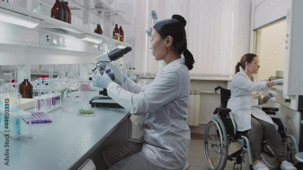 Slowmo tracking shot of diverse team of chemists doing research in lab They are checking solutions in test tube and flasks and using microscope Slowmo tracking shot of diverse team of chemists doing research in lab They are checking solutions in test tube and flasks and using microscope
