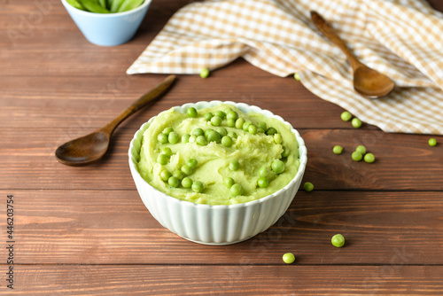 Bowl with mashed potatoes and green peas on wooden background
