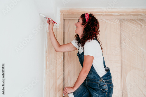 happy caucasian woman painting the room walls with white color. Do it yourself and new home concept photo