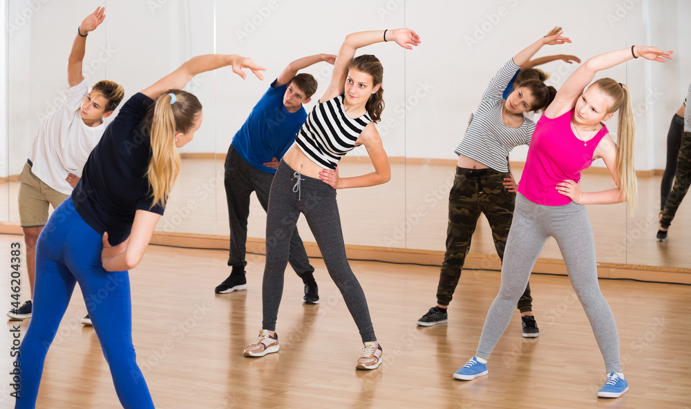 positive american teenage boys and girls with trainer stretching in dance hall