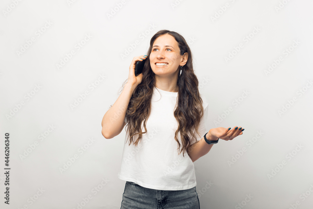 Portrait of a smiling young casual brunette woman talking on mobile phone over white background