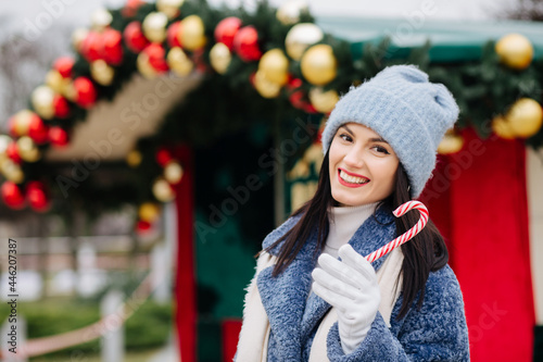 Cheerful young woman holding candy near the street Christmas deciration photo