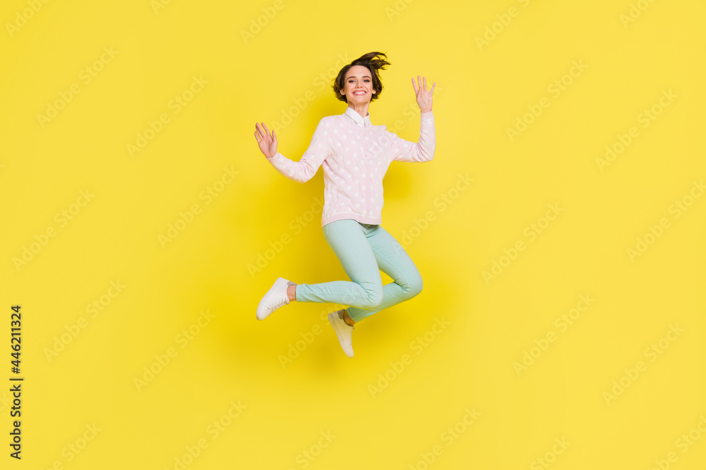Full length body size photo of cheerful model jumping up waving hands laughing isolated bright yellow color background