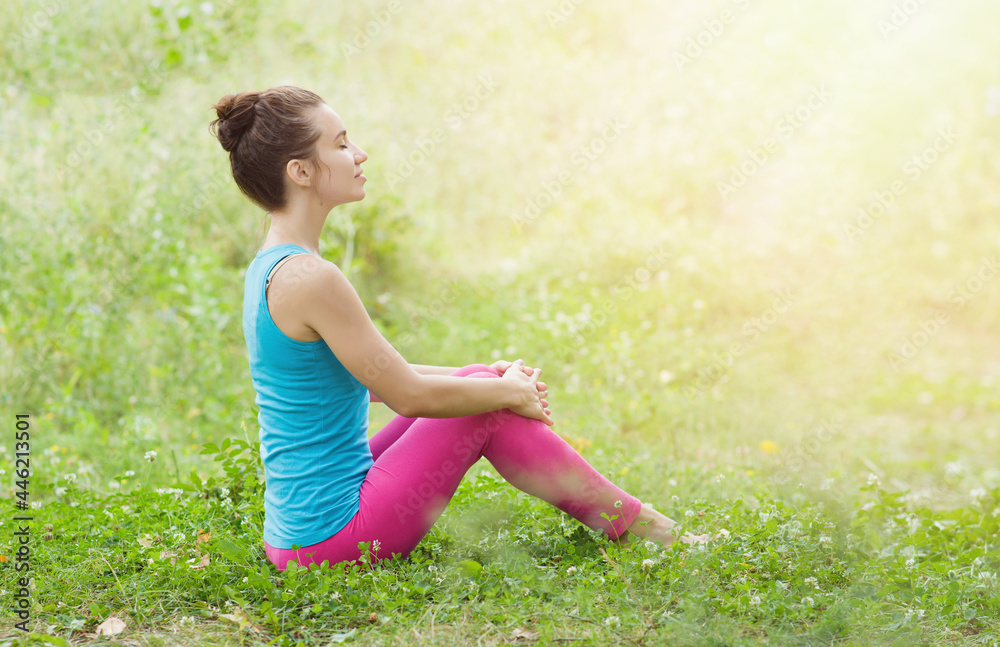 A young girl in bright sportswear is resting in the meadow after playing sports and enjoying life. Side view. Place for text A young girl in bright sportswear is resting in the meadow after playing sports and enjoying life. Side view. Place for text