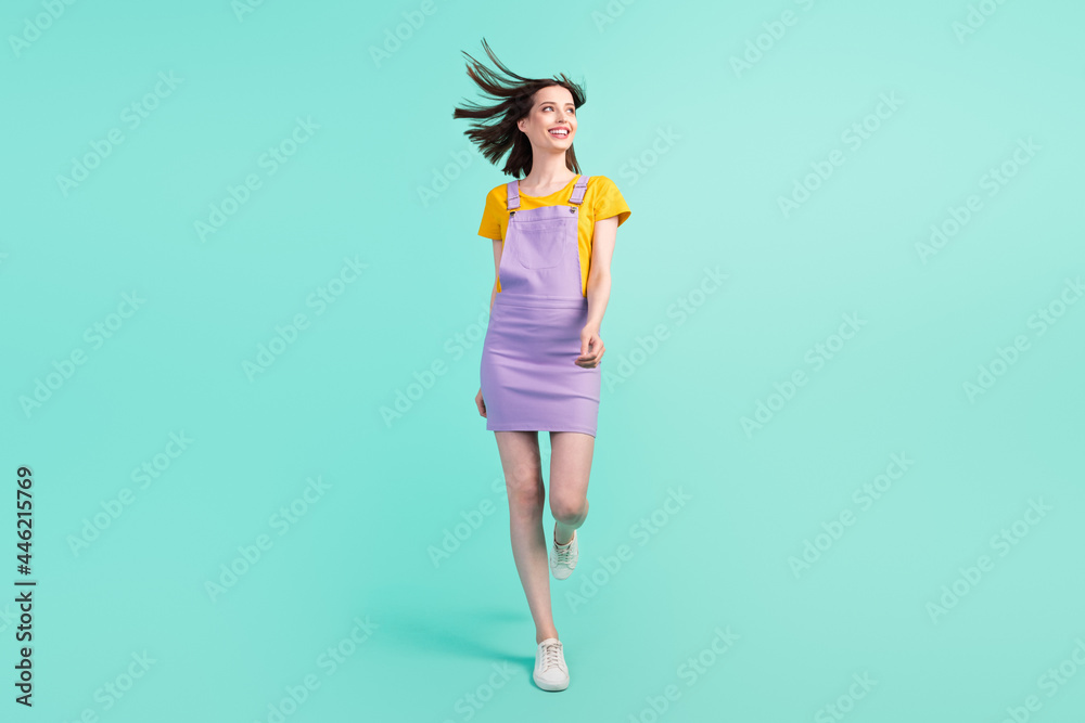 Full length photo of pretty charming young woman look empty space walk wind blow hair isolated on teal color background Full length photo of pretty charming young woman look empty space walk wind blow hair isolated on teal color background